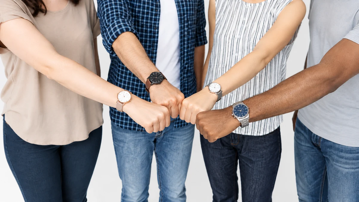 Quatre personnes réunissent leurs poings, avec leurs montres visibles au poignet.